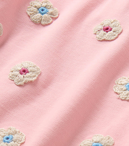 Close-up of cream crochet-style flower appliques with blue and pink centers on pink dress