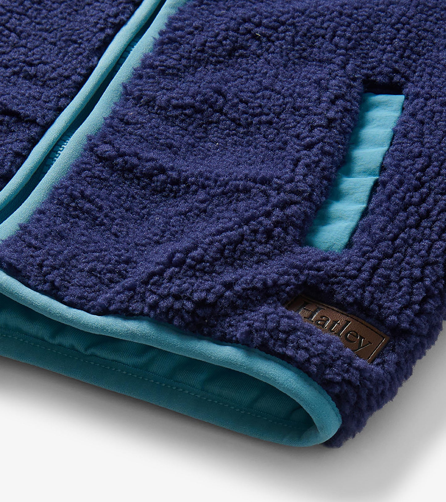 Close-up of patriot blue sherpa vest hem and pocket with light blue trim and visible Hatley logo patch