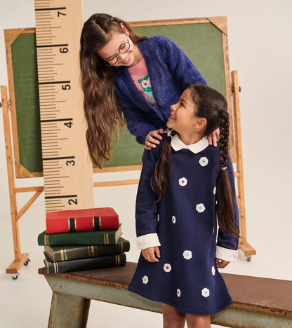 Girl modeling a navy dress with white collar and cuffs, shown from the front in a classroom-inspired setting