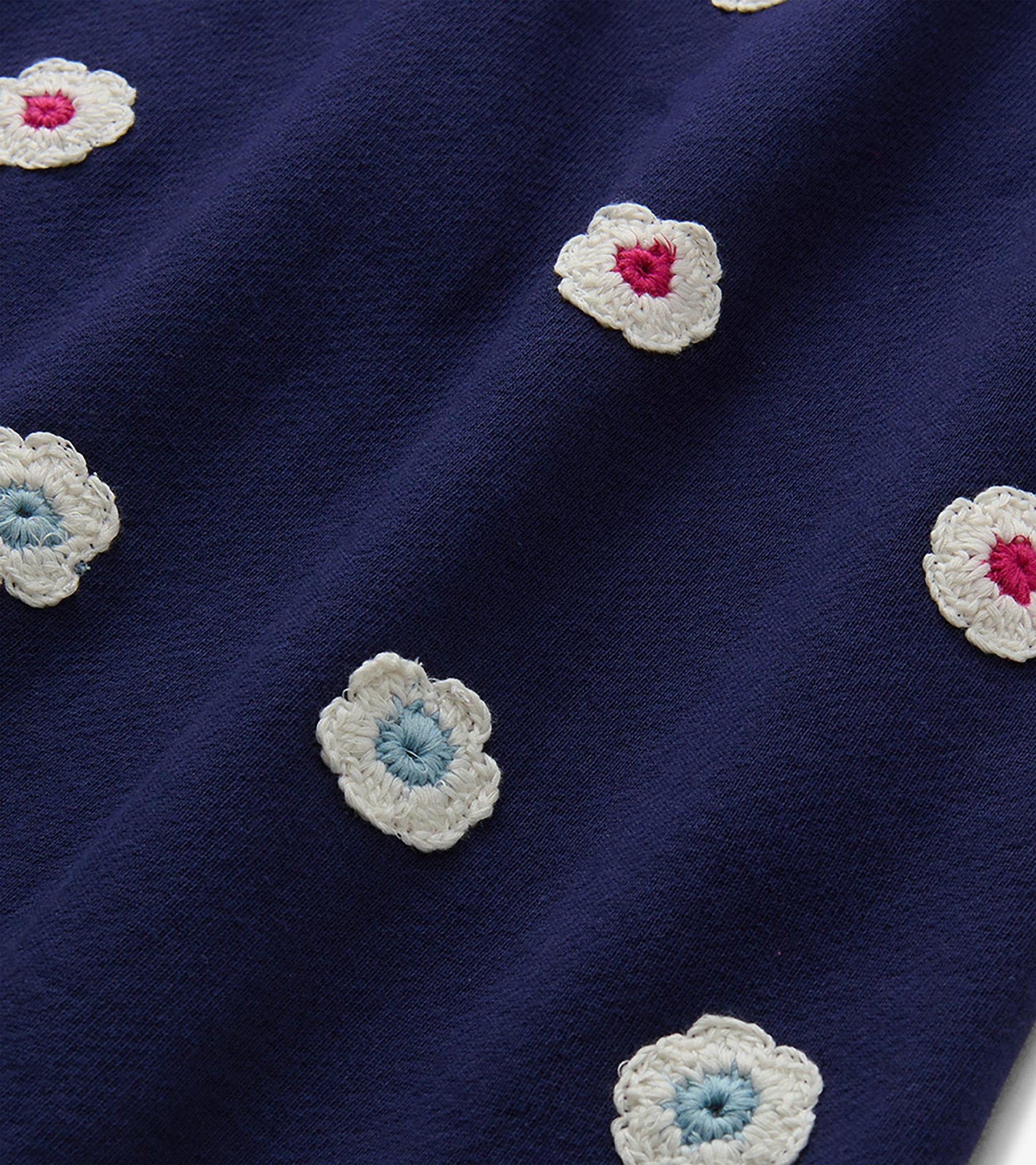 Close-up of patriot blue dress fabric with scattered cream crochet flowers in pink and light blue.