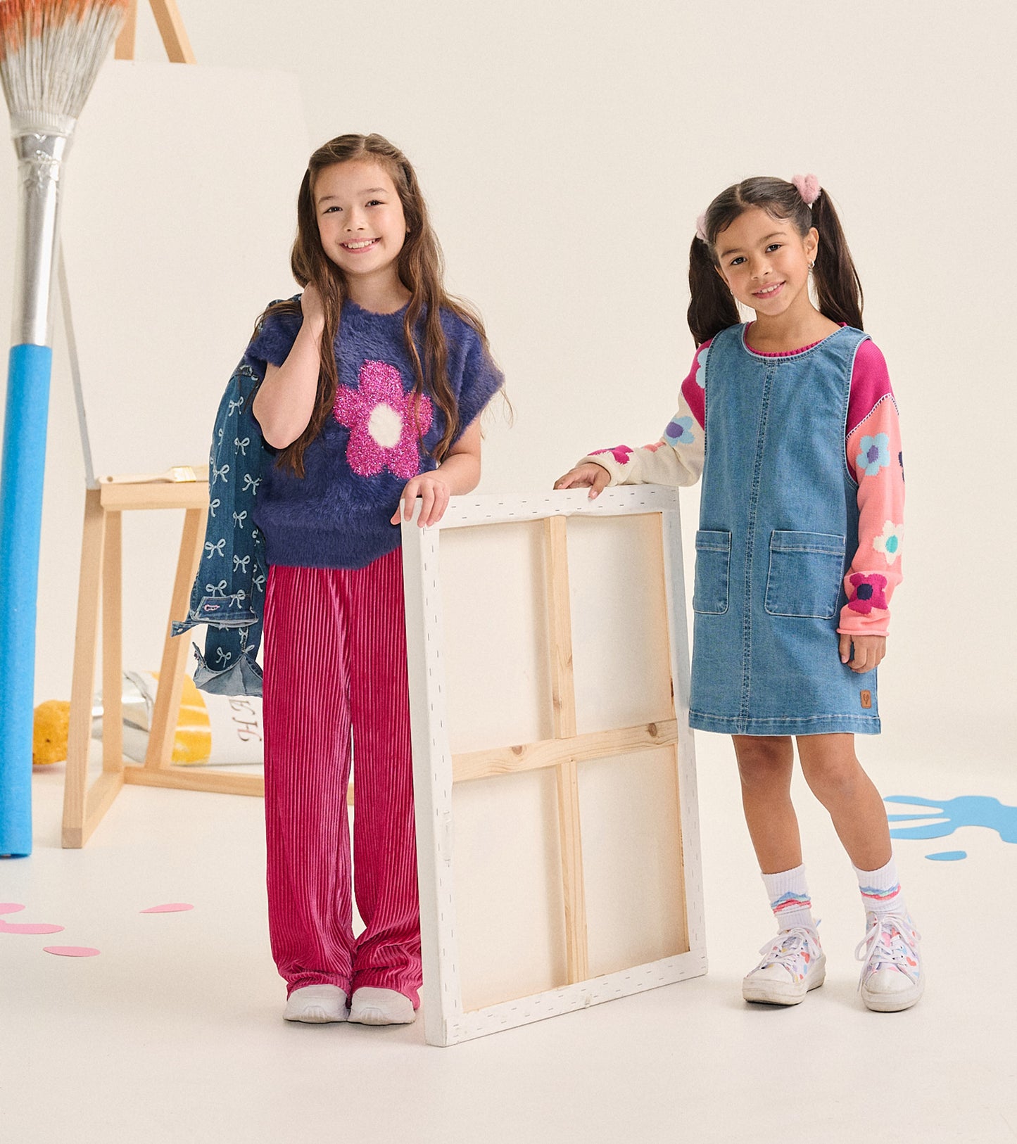 Girl wearing fuzzy blue flower sweater vest next to another child in a denim pinafore dress