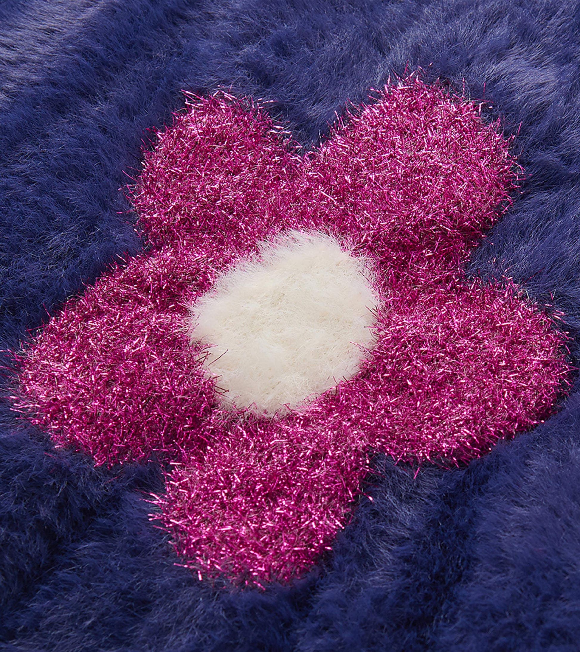 Close-up of bright pink flower detail with white center on the blue fuzzy sweater vest