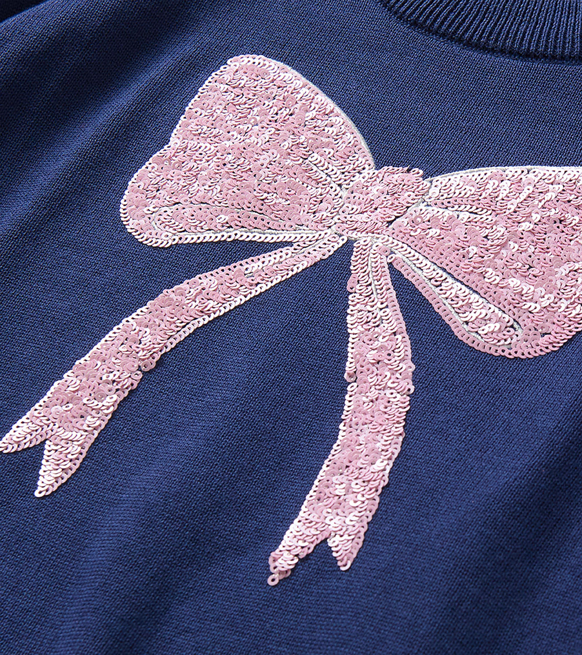 Close-up of the pink sequin bow detail on the front of the navy sweater