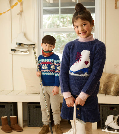 Girl wearing a patriot blue A-line skirt with gold snaps, styled with a fuzzy skate sweater and ice skates