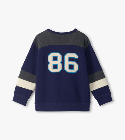 Back view of kids blue pullover top with gray yoke, cream sleeve stripes, and large 86 patch