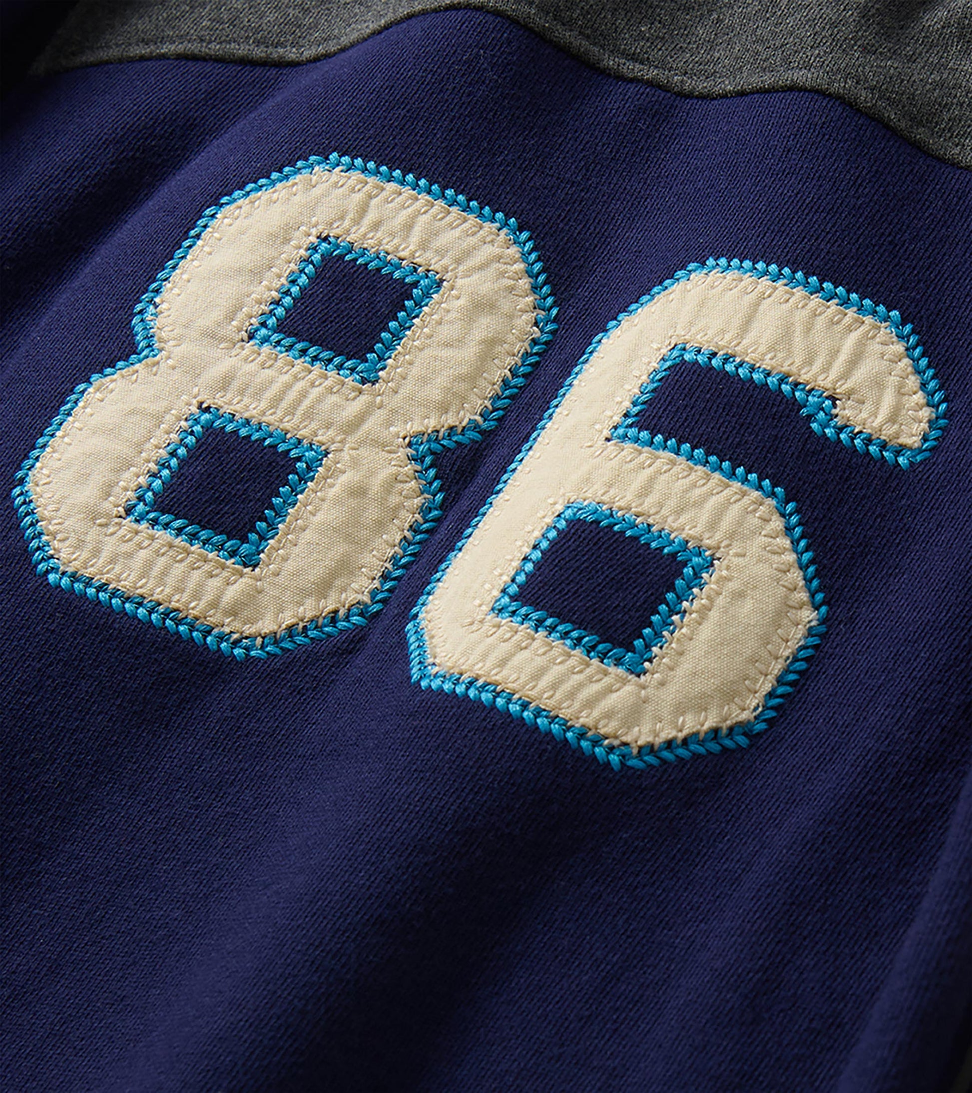 Close-up of cream 86 appliqué with bright blue stitching on patriot blue fabric