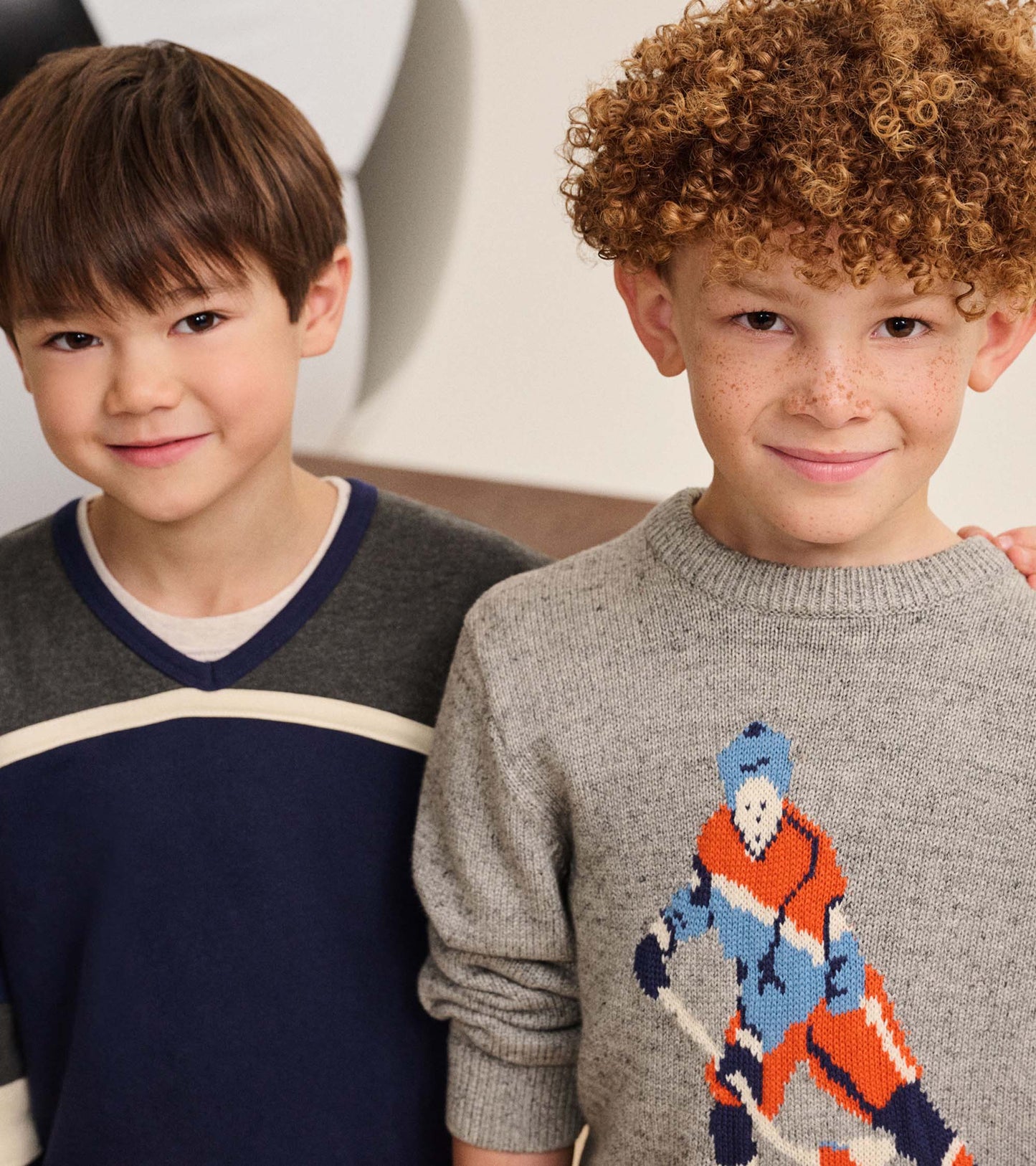 Boy wearing a patriot blue pullover with charcoal yoke, cream stripe, and V-neck, shown beside another child
