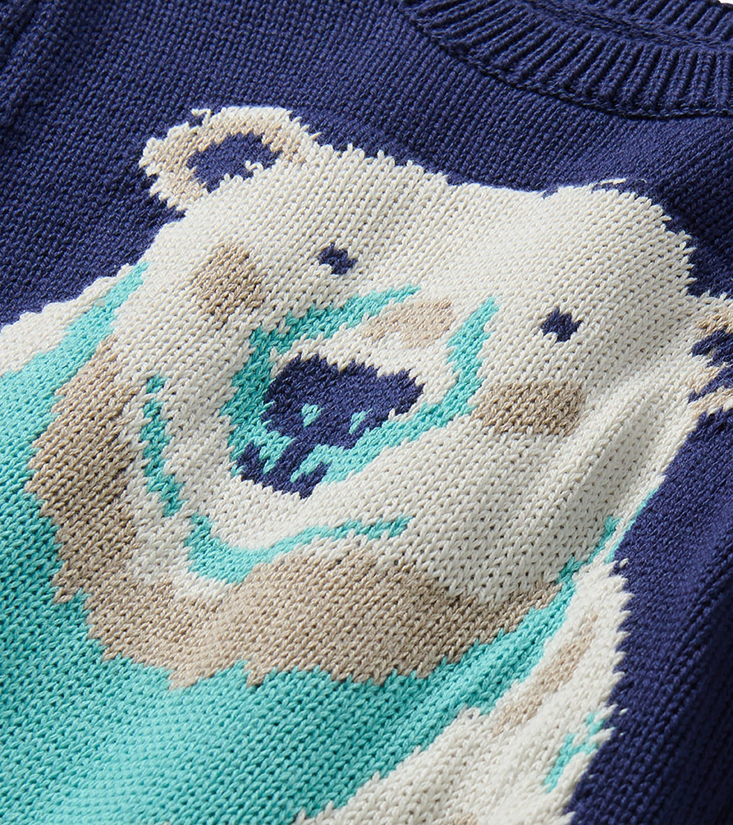 Close-up of polar bear knit graphic on navy sweater with bright teal scarf detail