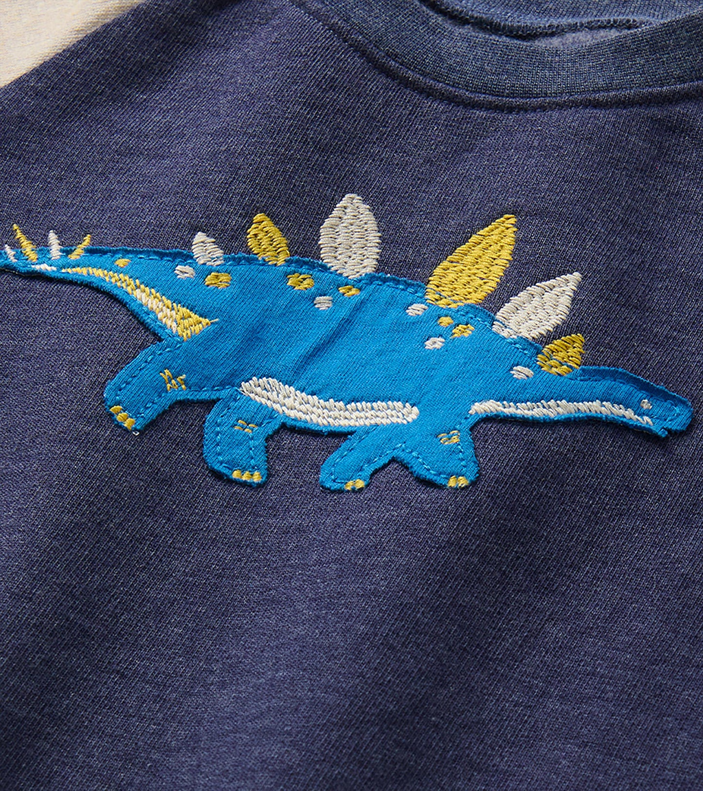 Close-up of blue stegosaurus applique with white and yellow embroidered details on the navy sweatshirt chest