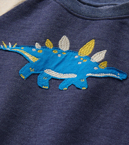 Close-up of blue stegosaurus applique with white and yellow embroidered details on the navy sweatshirt chest