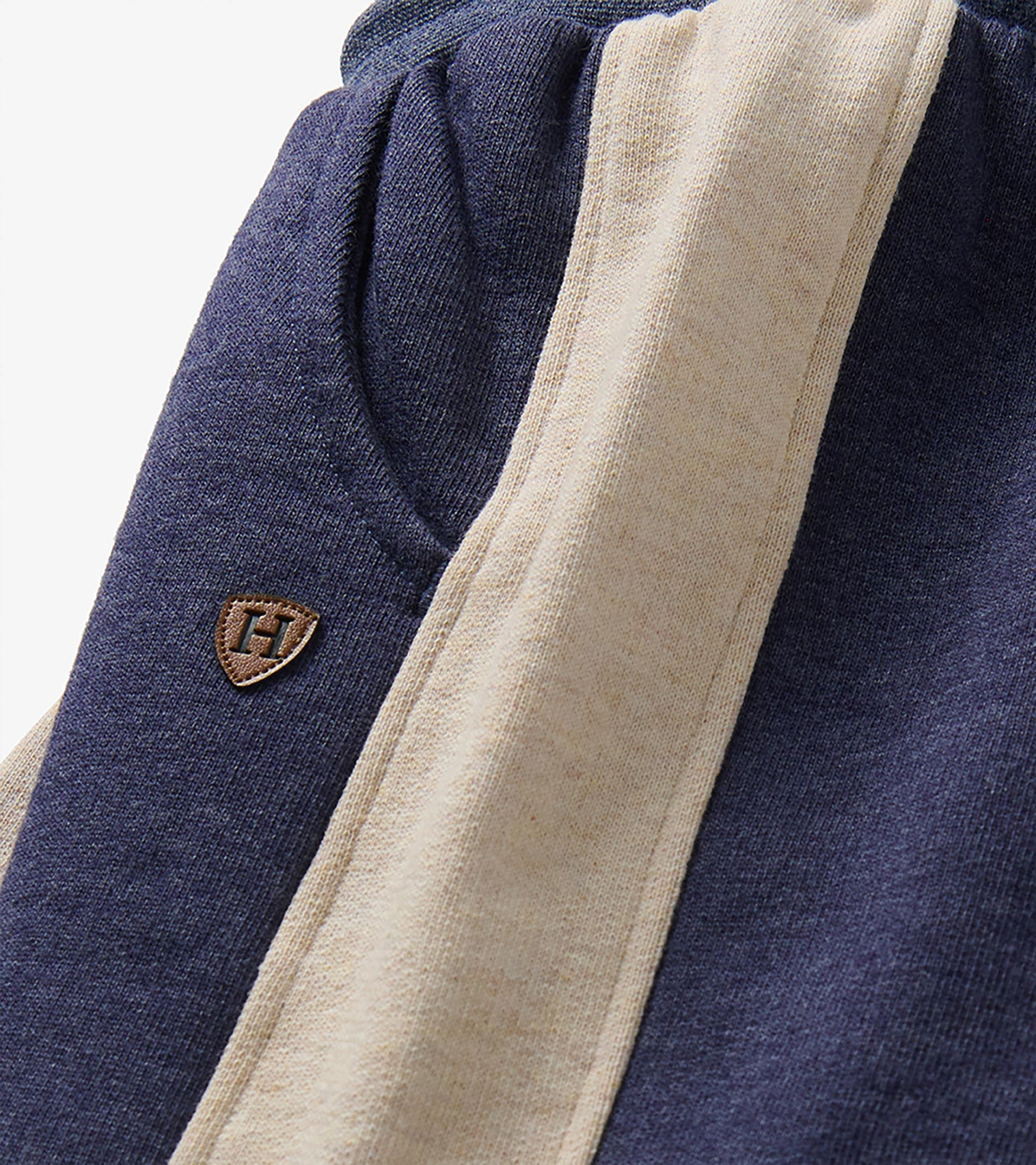 Close-up of blue melange track pants with oatmeal side panel, pocket seam, and small H patch