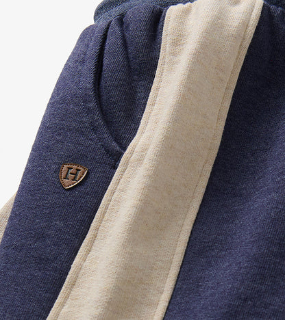 Close-up of blue melange track pants with oatmeal side panel, pocket seam, and small H patch