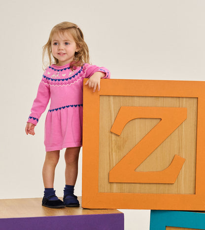 Toddler wearing a bright pink sweater dress with navy heart bands and cream puppy motifs on the yoke