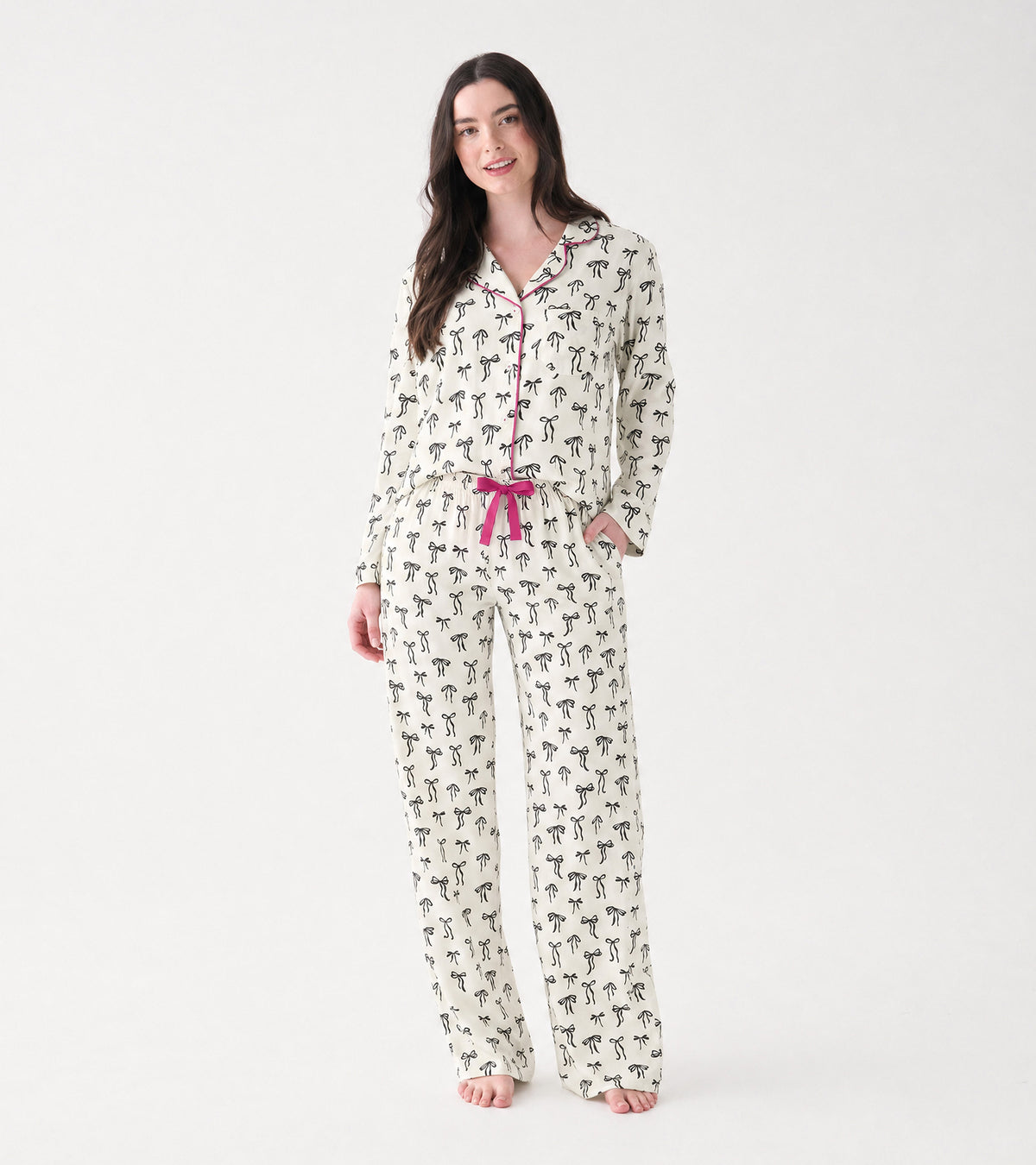 Women's pajama set with cream ribbon bow print, pink piping, and matching pink drawstring, shown on model