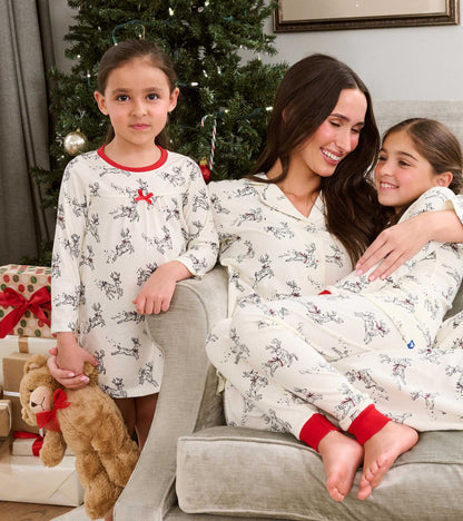 Girl wearing white reindeer print nightdress with red neckline beside family in matching holiday pajamas