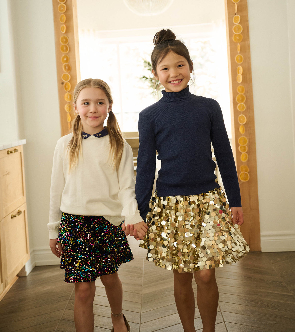 Girl wearing a navy rainbow sequin flounce skirt with a cream sweater, standing beside another girl