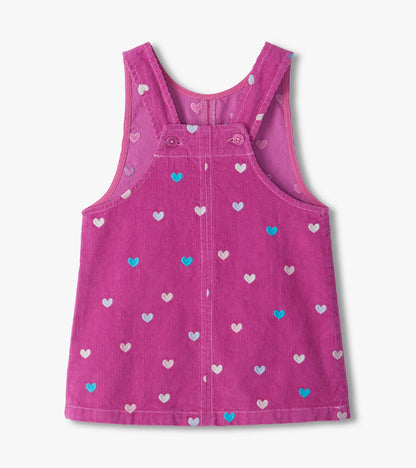 Back view of pink pinafore dress with embroidered hearts, crossed shoulder straps, and button fastening