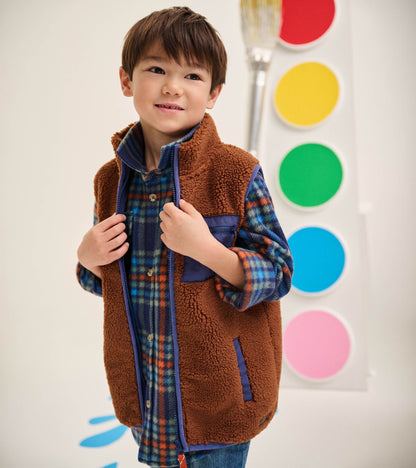 Boy wearing a brown sherpa vest with blue trim and blue chest pocket over a blue plaid shirt