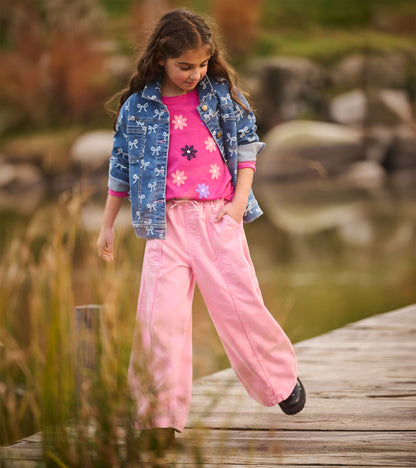 Girl wearing the berry pink flower graphic T-shirt under a blue bow-print jacket with light pink pants