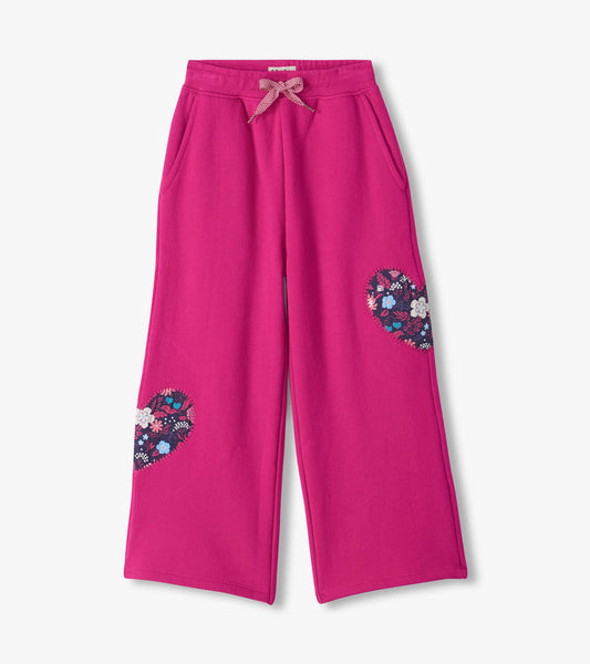 Berry pink wide leg track pants with side pockets, drawstring waist, and floral heart patches on the legs