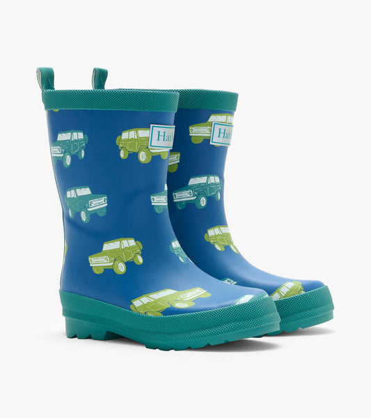 Pair of blue kids rain boots with green trim and vintage truck print, angled front view