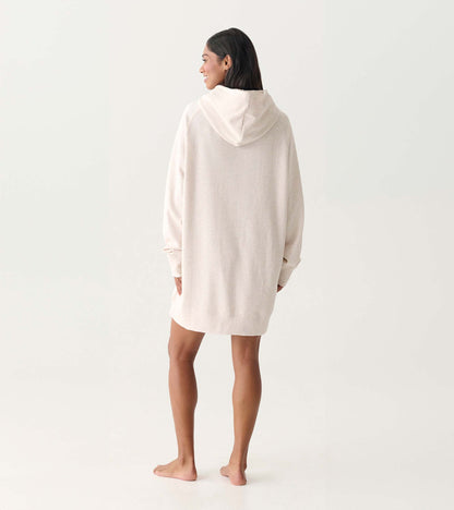 Back view of an oversized cream hoodie dress with a hood and long sleeves, worn by a model barefoot.