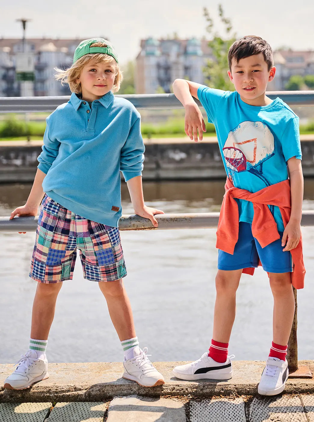 Promotes the boys collection. Showing two boys modeling bright casual outfits by a waterfront railing. With "Boys" text.
