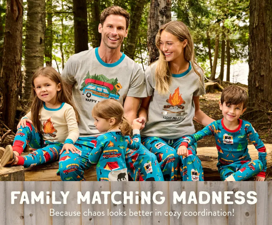 Promotes family matching sleepwear. Showing family of four in coordinated camping-themed pajamas sitting in a forest.