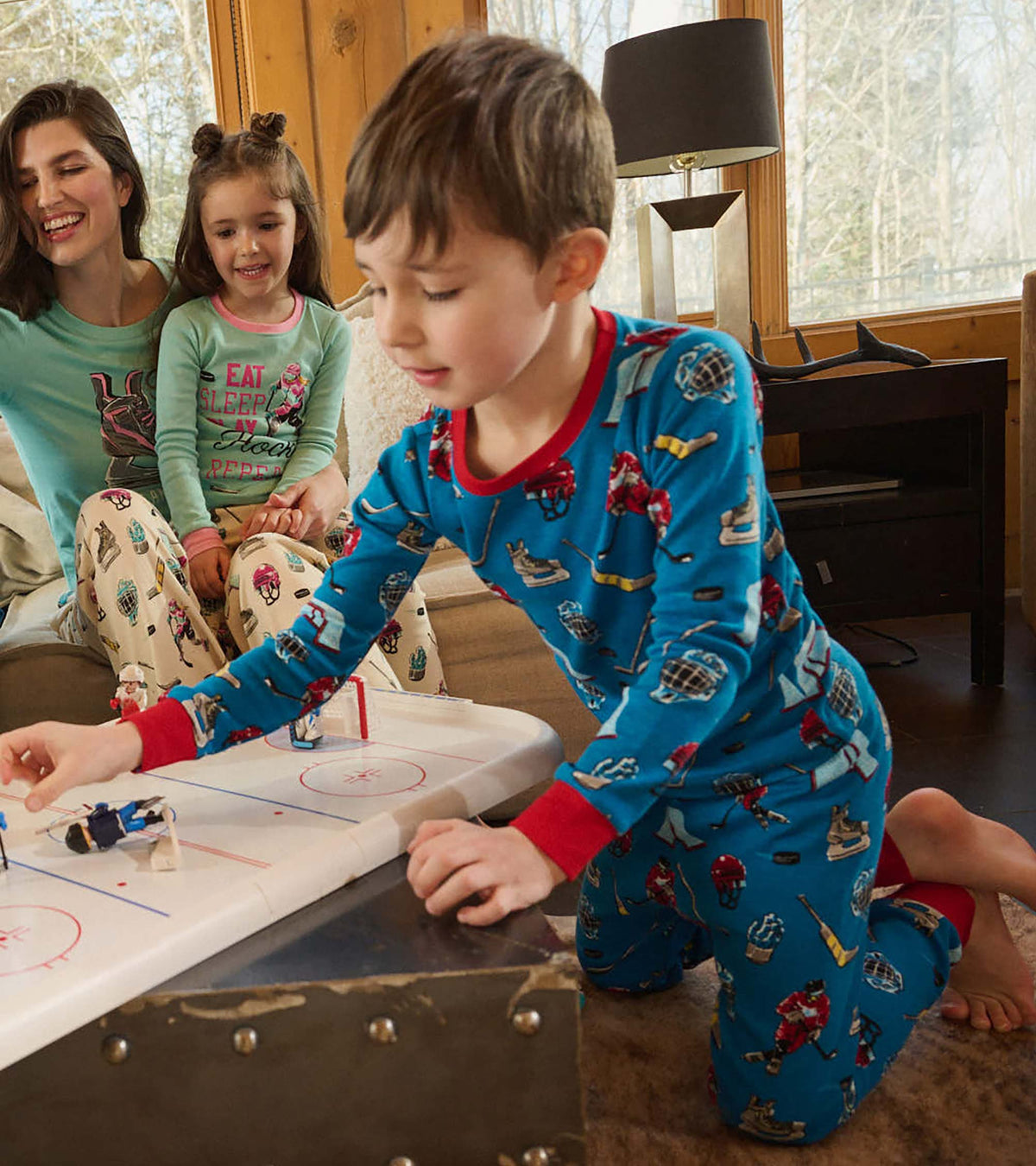 Child wearing blue hockey print pajamas with red trim while playing tabletop hockey indoors