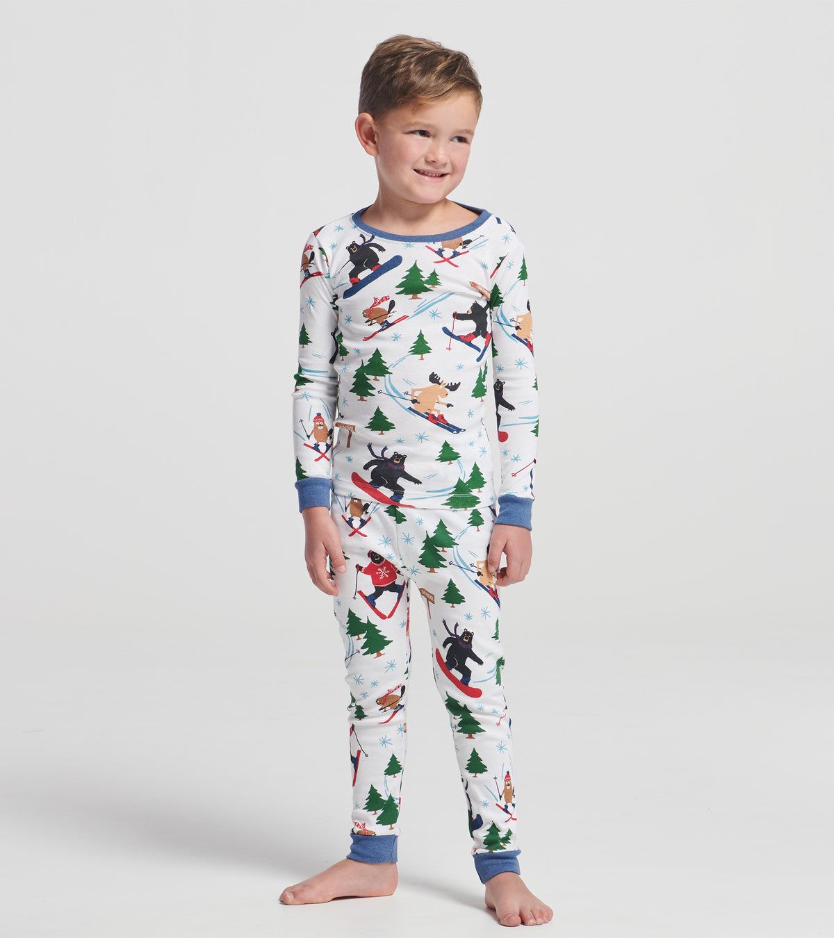 Child wearing white ski print pajama set with blue trim, trees, snowflakes, and skiing animals