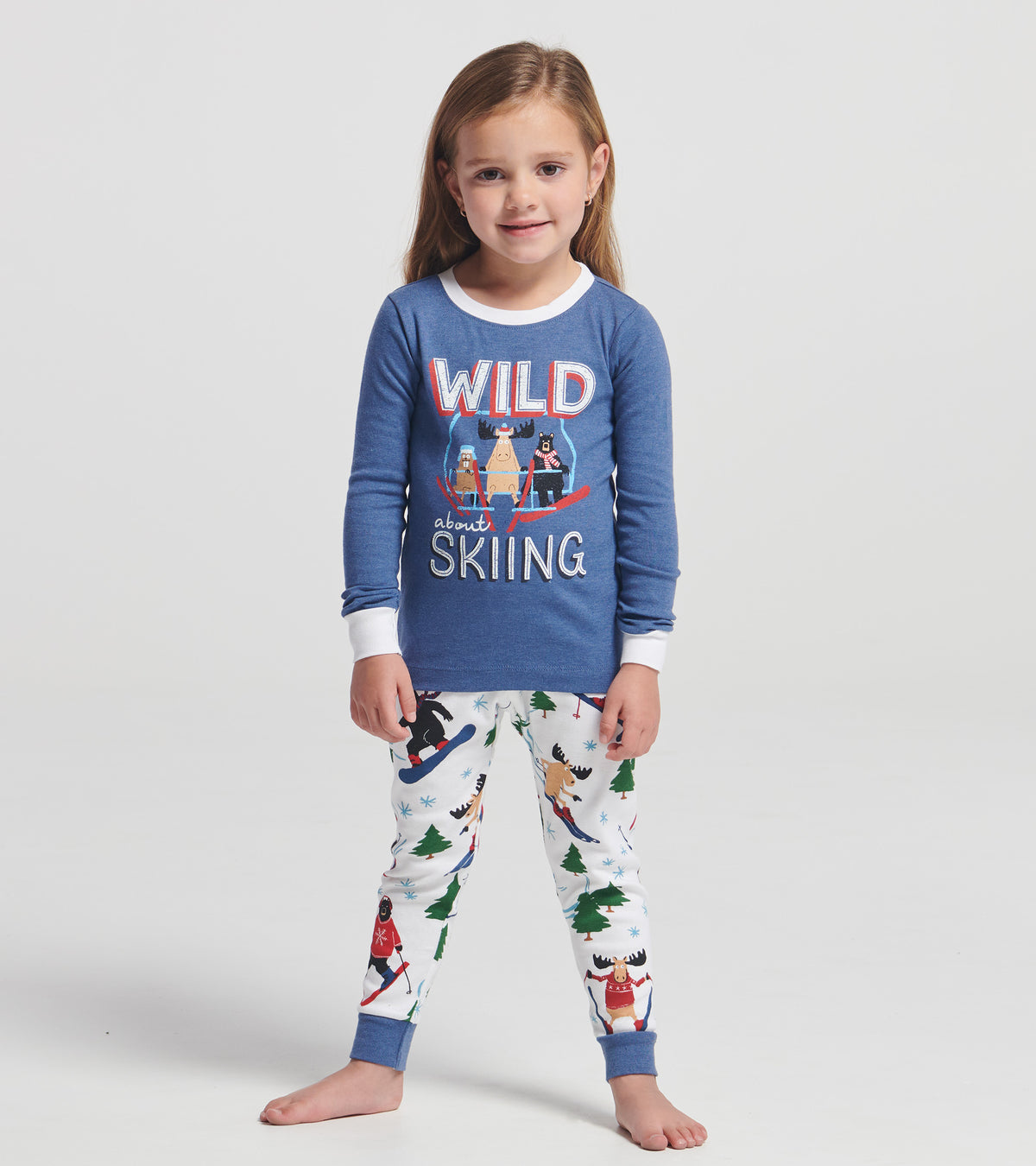 Girl modeling blue kids pajama set with wild about skiing graphic top and white animal ski print pants