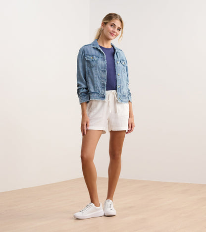 Blue acid wash linen jacket with a cropped fit, featuring front pockets and a button closure, styled with white shorts.
