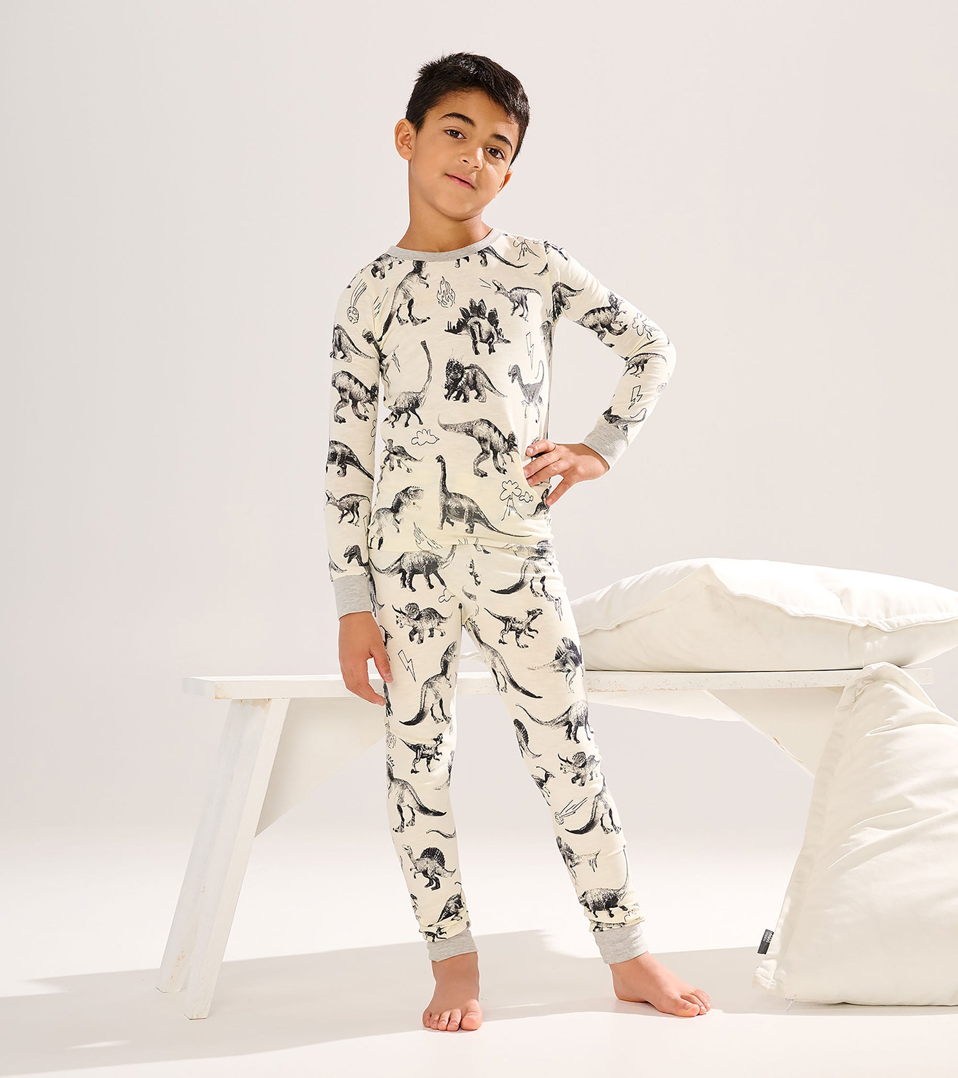 Cream long-sleeve pajama set with black dinosaur print, gray cuffs, shown on a boy standing barefoot