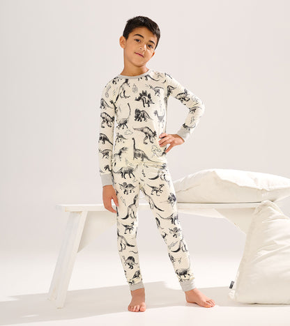 Cream long-sleeve pajama set with black dinosaur print, gray cuffs, shown on a boy standing barefoot