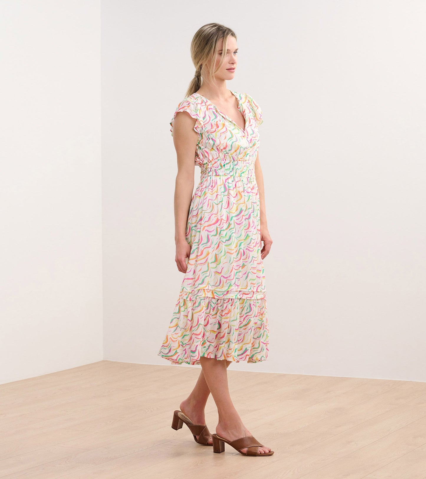 Midi dress featuring wavy stripes in pastel colors, with a V-neck and ruffled sleeves, styled with heeled sandals.