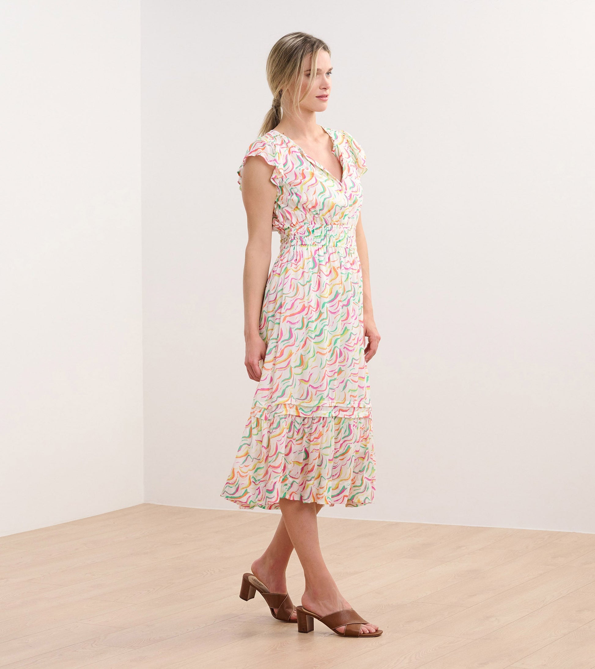 Midi dress featuring wavy stripes in pastel colors, with a V-neck and ruffled sleeves, styled with heeled sandals.