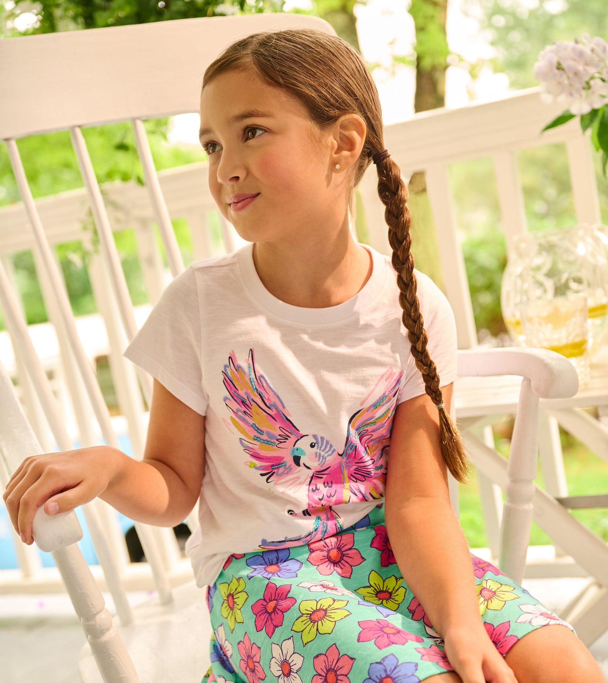 White short-sleeve tee featuring a colorful parrot graphic, paired with a floral-patterned skirt.