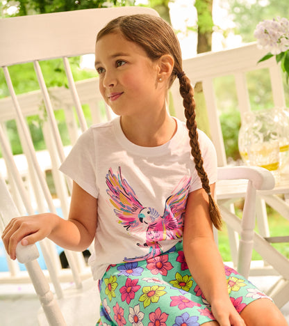 White short-sleeve tee featuring a colorful parrot graphic, paired with a floral-patterned skirt.