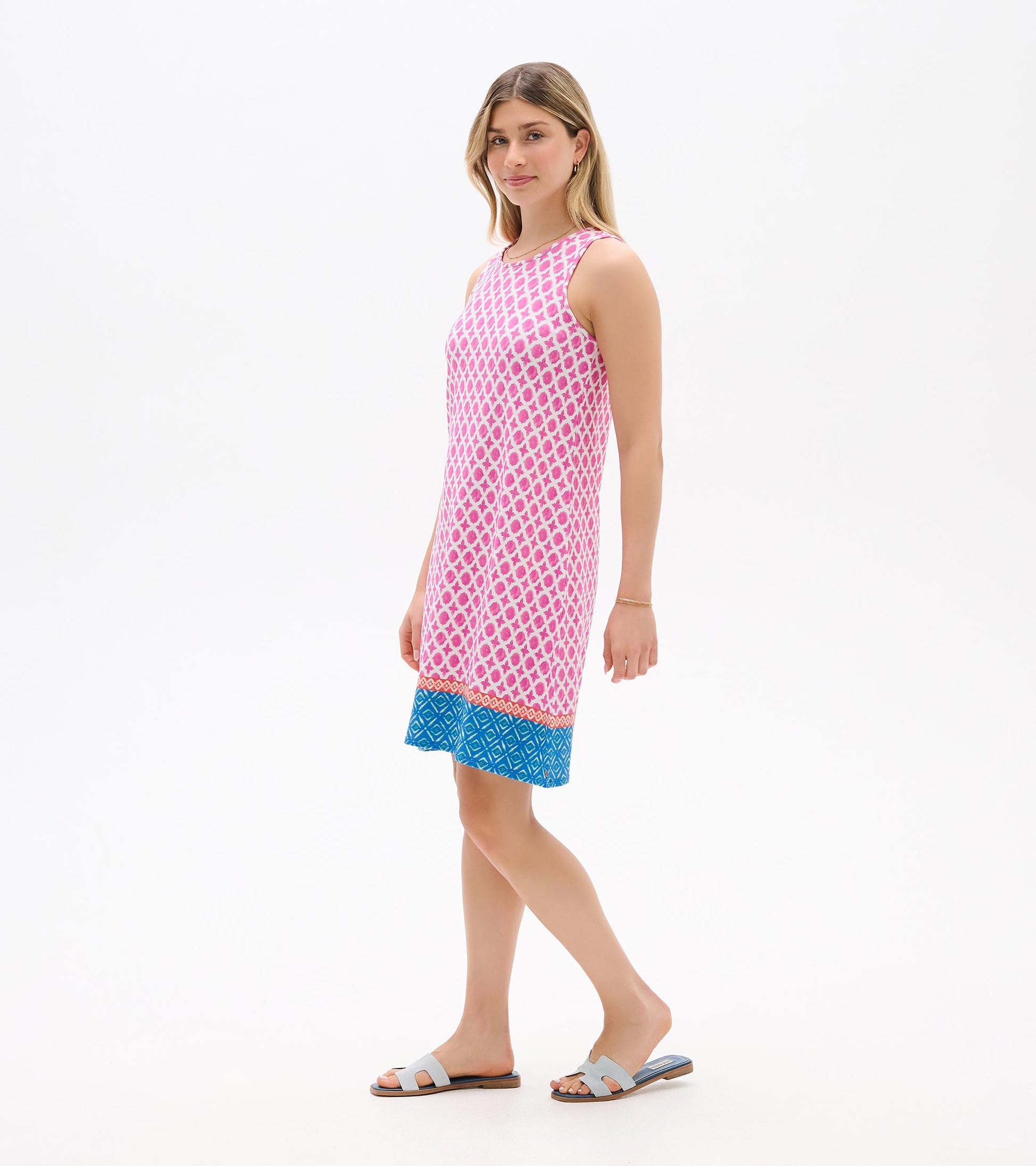Sleeveless pink patterned shift dress with blue hem, shown on model in side view