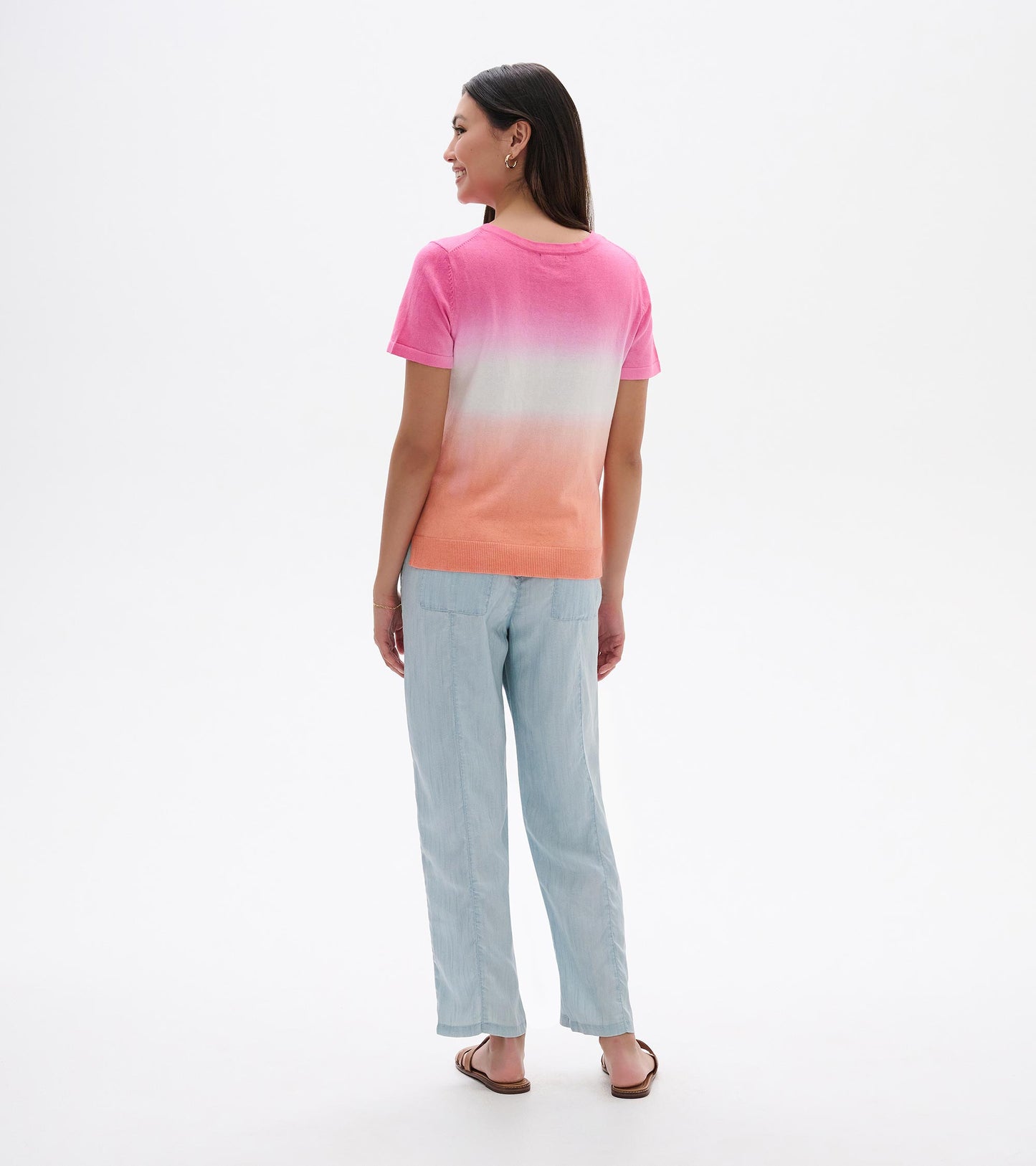 Back view of a pink-to-coral dip-dye knit tee with short sleeves and a crew neck, worn with light blue pants.