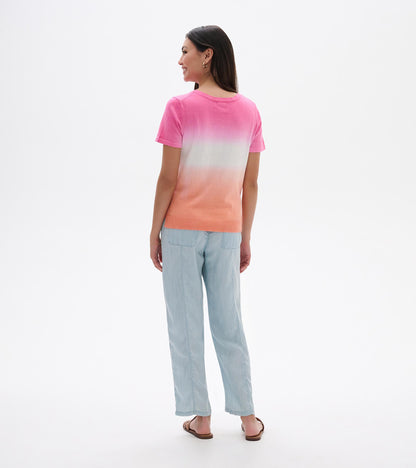 Back view of a pink-to-coral dip-dye knit tee with short sleeves and a crew neck, worn with light blue pants.