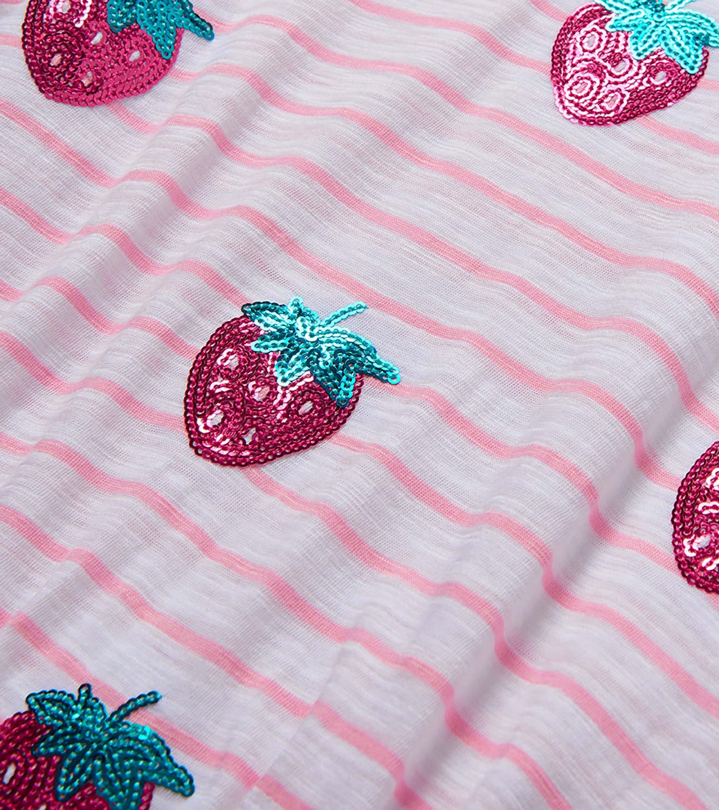 White girls dress fabric with pink stripes and sequined strawberry pattern close-up