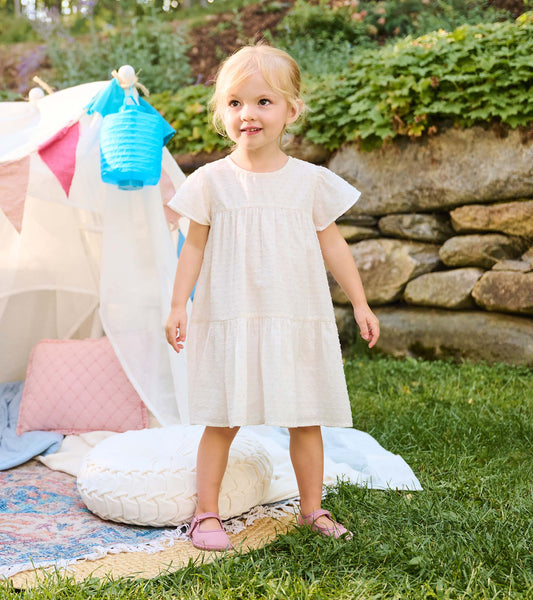 Toddler girl wearing a pearl Swiss dot dress with flutter sleeves and a tiered skirt outdoors