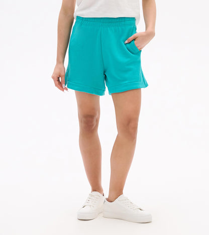 Turquoise pull-on shorts with elastic waistband, side pockets, and cuffed hems, worn with white sneakers.