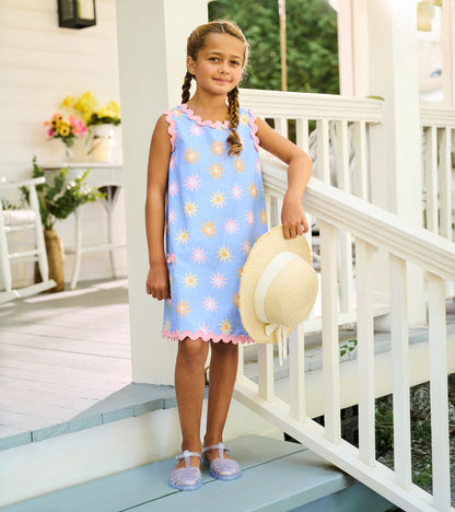 Girl wearing a blue pinafore dress with faded sun print, pink rickrack trim, and scalloped hem