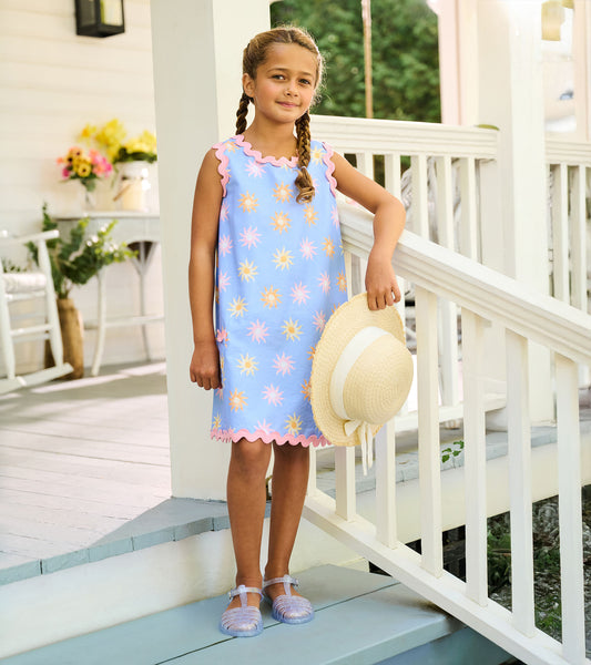 Girl wearing a blue pinafore dress with faded sun print, pink rickrack trim, and scalloped hem