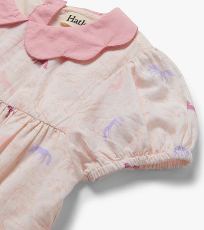 Close-up of a pale pink baby dress with a scalloped collar and pastel pony print, gathered sleeve cuff