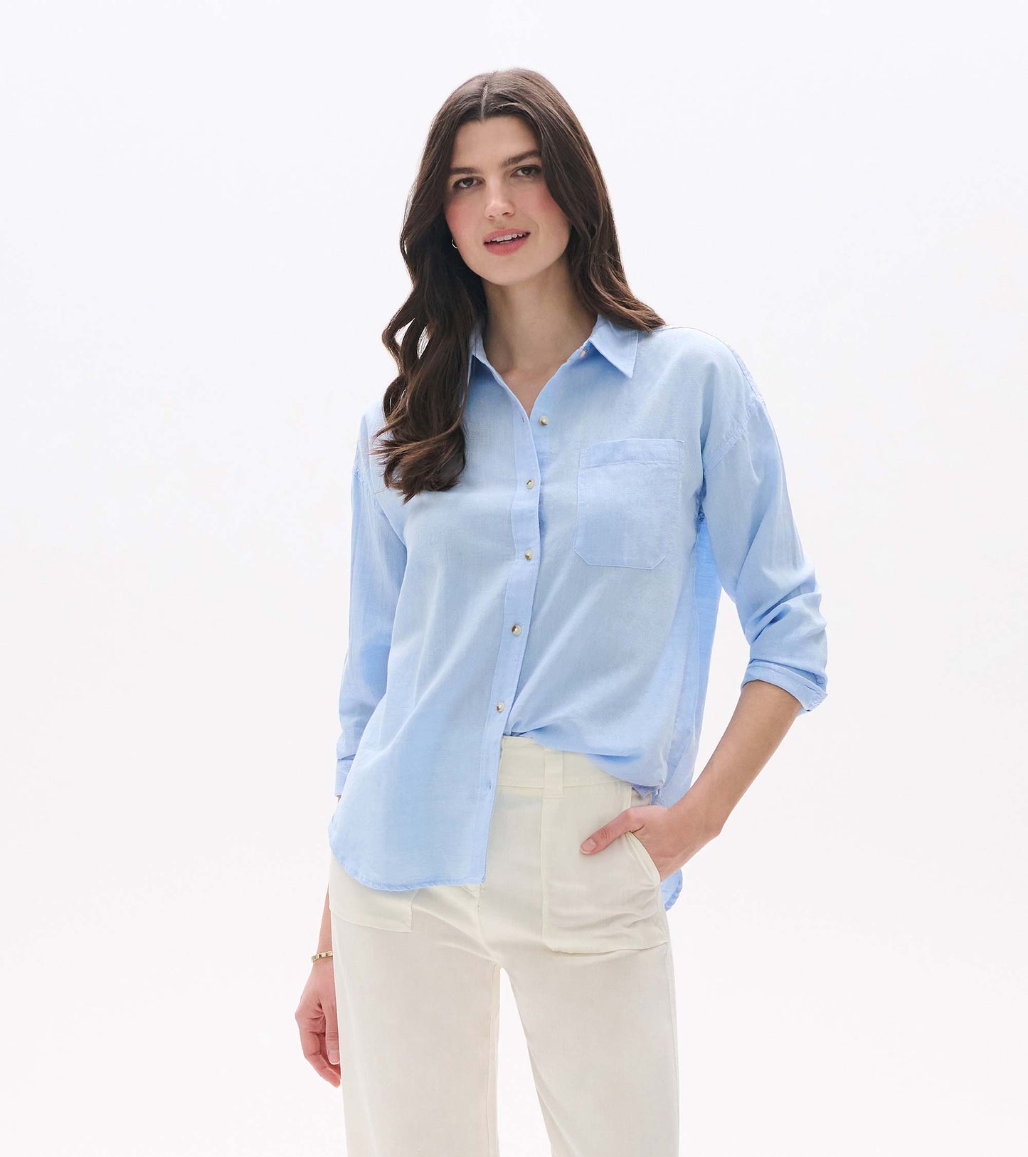 Light blue chambray button-down shirt with collar, chest pocket, and long sleeves, worn with cream pants.