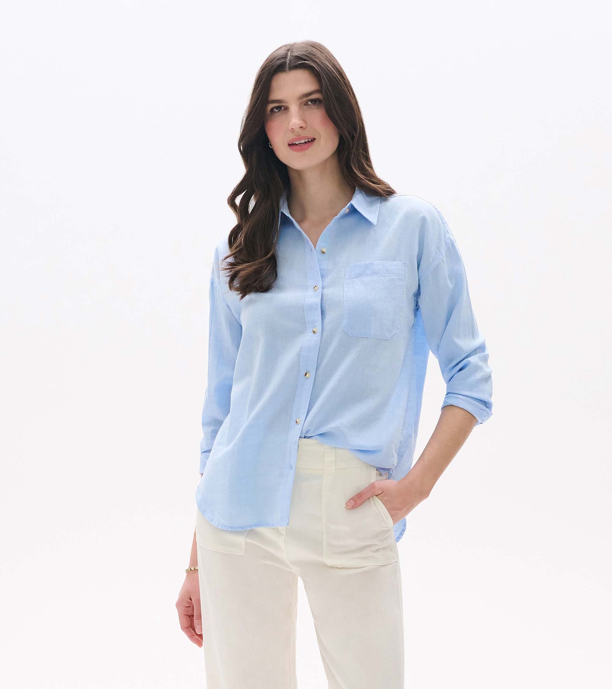 Light blue chambray button-down shirt with collar, chest pocket, and long sleeves, worn with cream pants.