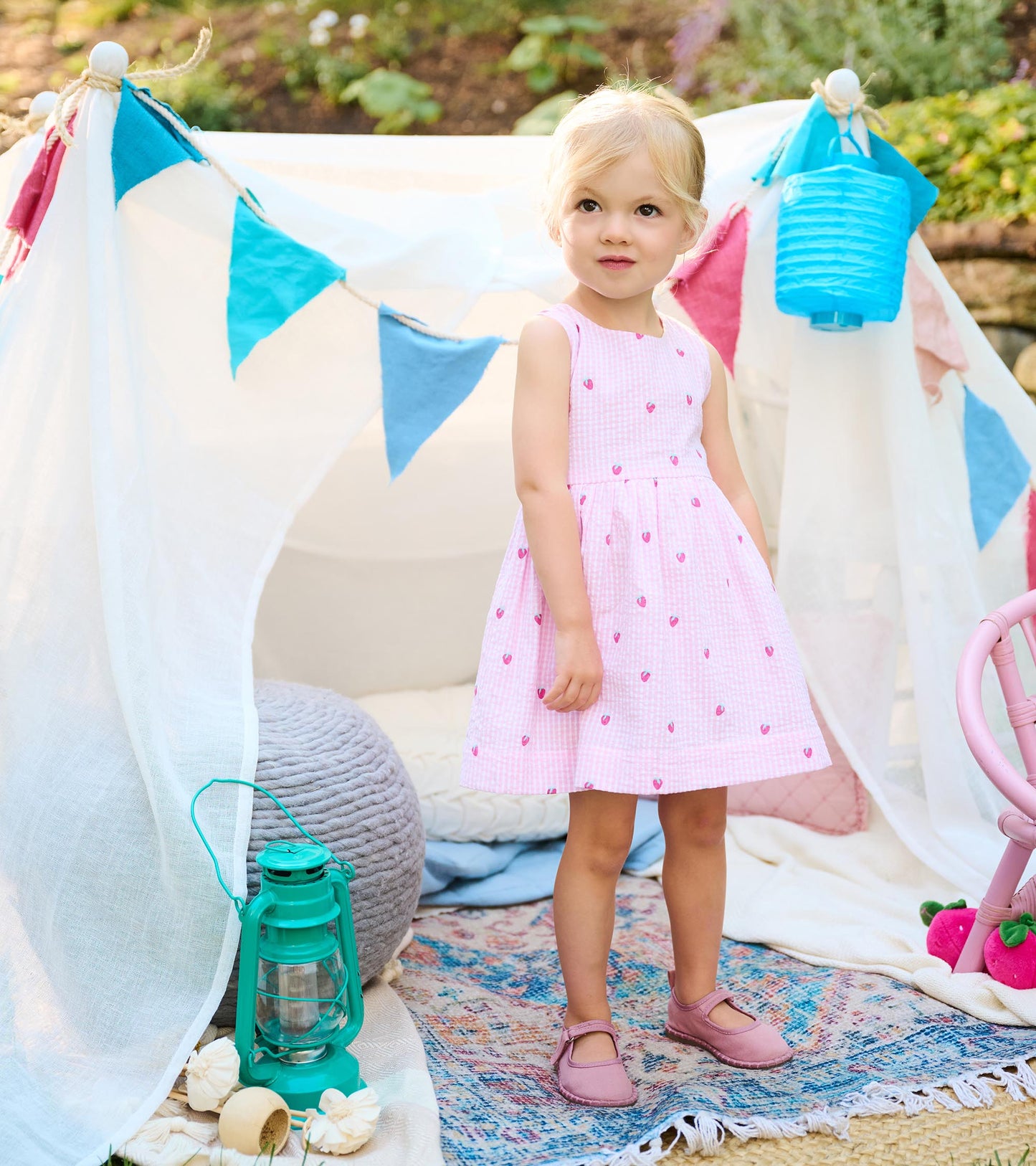Toddler wearing a sleeveless pink gingham dress with small strawberry motifs and a gathered skirt